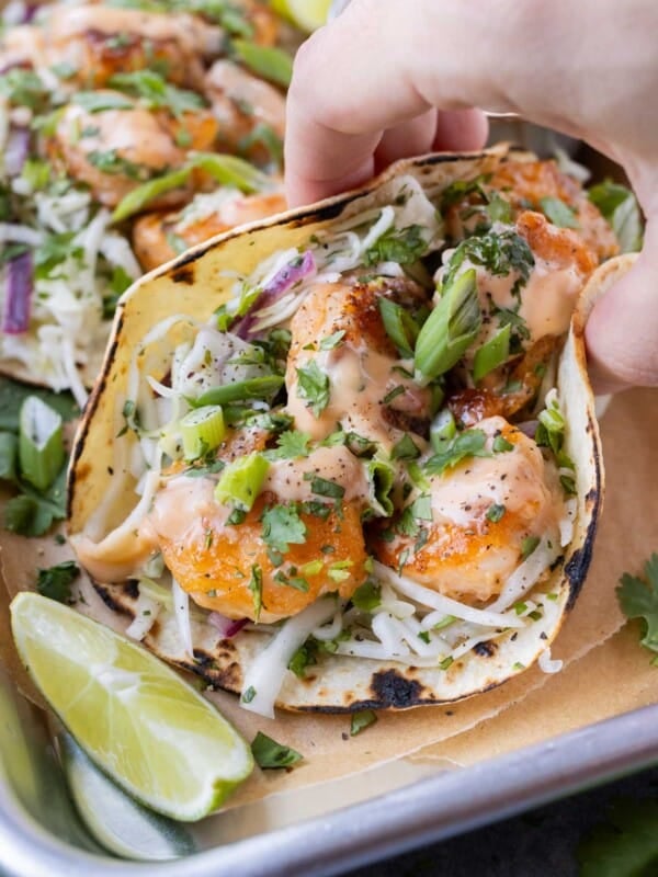 A Bang Bang Shrimp Taco with slaw is being picked up from a serving tray.