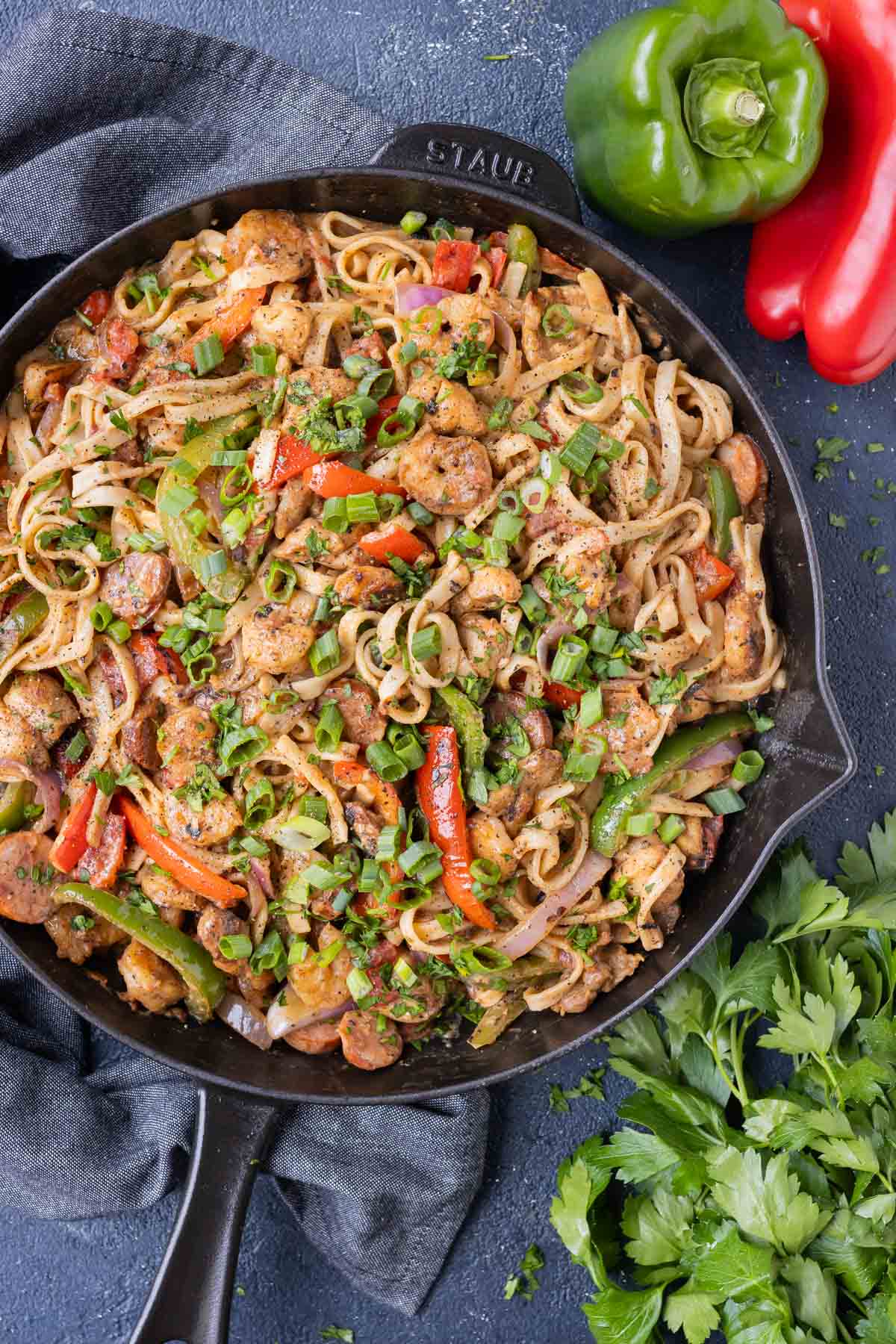 A creamy Cajun pasta dish with chicken, shrimp, and sausage is cooked in a cast iron skillet.