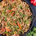 A cast-iron skillet is full of a creamy Cajun Jambalaya pasta recipe with chicken, andouille sausage, shrimp, bell peppers and onions.