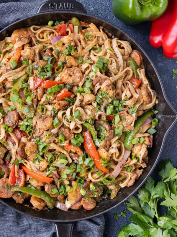 A cast-iron skillet is full of a creamy Cajun Jambalaya pasta recipe with chicken, andouille sausage, shrimp, bell peppers and onions.