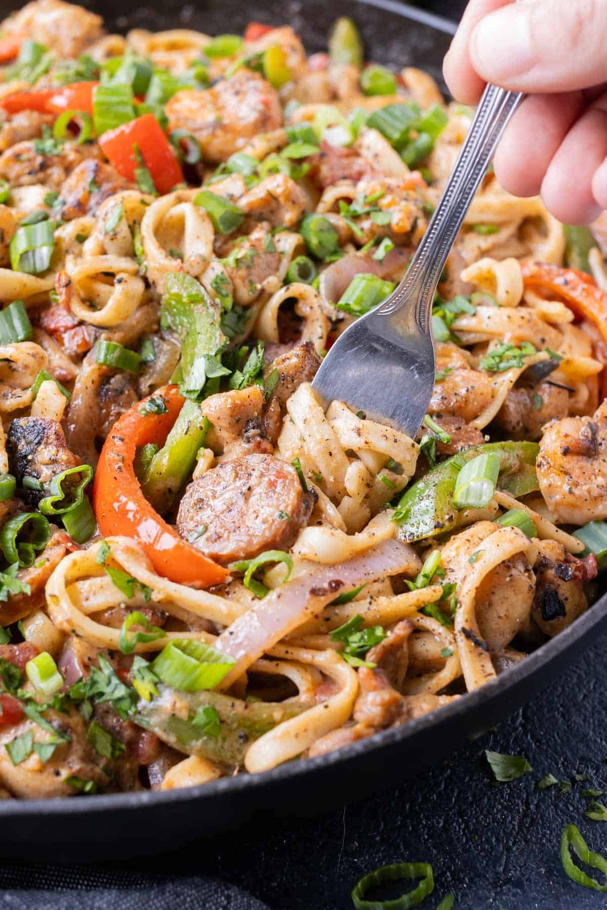 A fork digs into a bowl of Creamy Cajun Pasta with chicken, shrimp, and sausage.