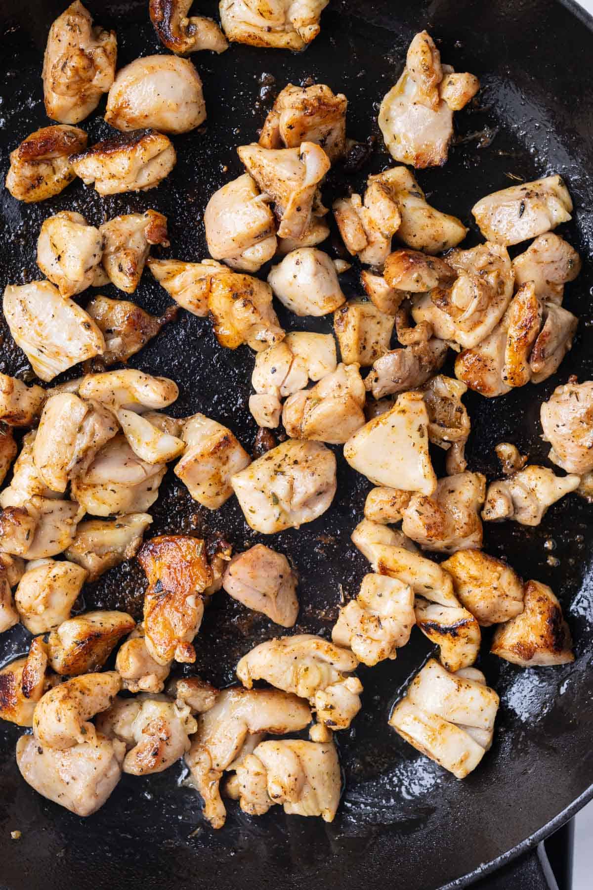 Seasoned chicken is cooked in a cast iron skillet.
