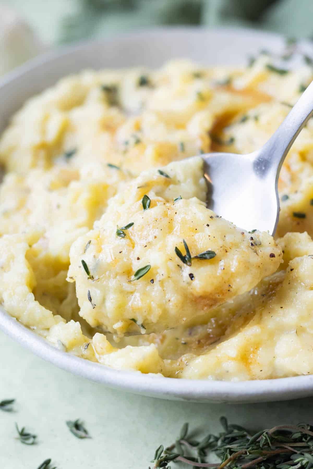 A spoon digs into a bowl full of brown butter mashed potatoes.