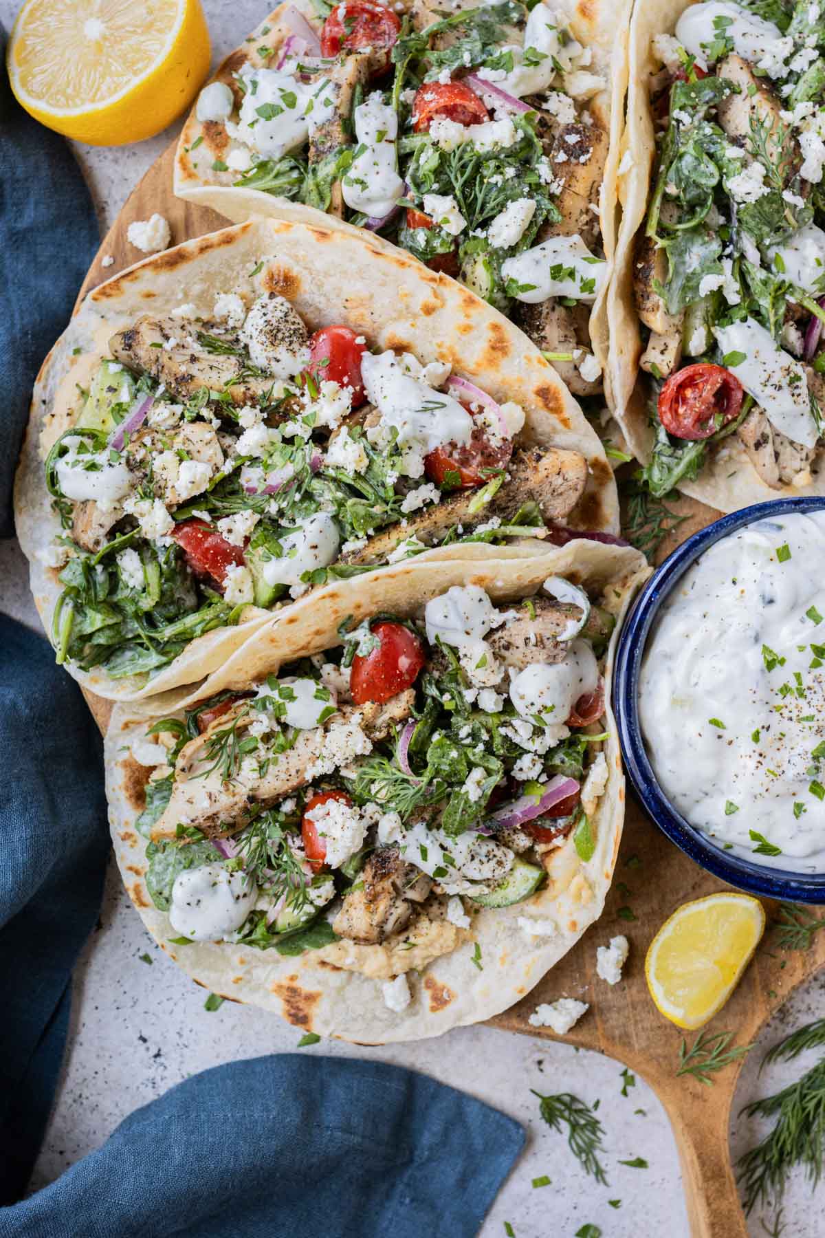Several tacos filled with Greek chicken and salad are served on a tray.