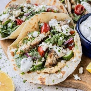 Greek Chicken Tacos with a Tomato Cucumber and Arugula Salad tossed in tzatziki sauce are served on flour tortillas on a tray.