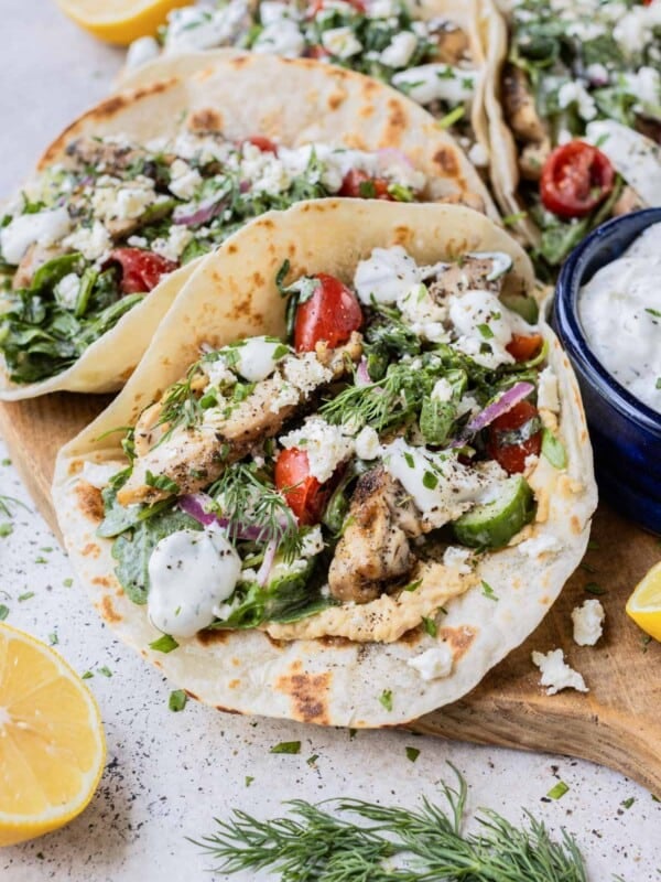 Greek Chicken Tacos with a Tomato Cucumber and Arugula Salad tossed in tzatziki sauce are served on flour tortillas on a tray.