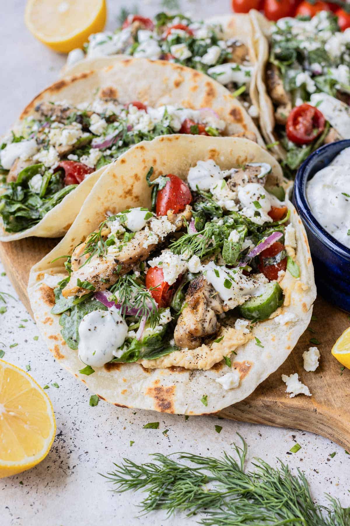 Greek Chicken Tacos with a Tomato Cucumber and Arugula Salad tossed in tzatziki sauce are served on flour tortillas on a tray.