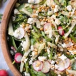 Grilled fennel asparagus salad with asparagus, feta, and pine nuts are in a large salad bowl being tossed in a shallot vinaigrette.