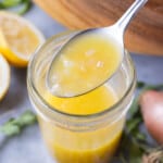 A spoon is scooping a homemade shallot vinaigrette dressing with Dijon and lemon juice from a mason jar.