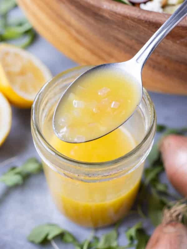 A spoon is scooping a homemade shallot vinaigrette dressing with Dijon and lemon juice from a mason jar.