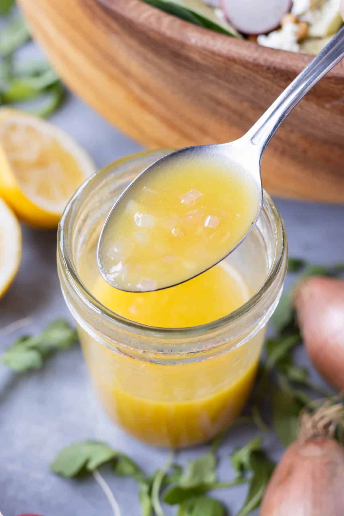 A spoon is scooping a homemade shallot vinaigrette dressing with Dijon and lemon juice from a mason jar.