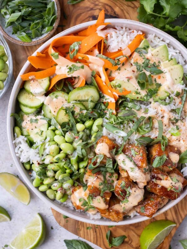 Rice, veggies, and bang bang salmon are served in a white bowl surrounded by fresh ingredients for an easy summer dinner recipe.