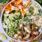 Bang bang salmon bowls are on a wooden serving board with cilantro and limes around it.
