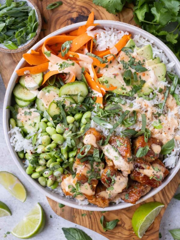 Bang bang salmon bowls are on a wooden serving board with cilantro and limes around it.