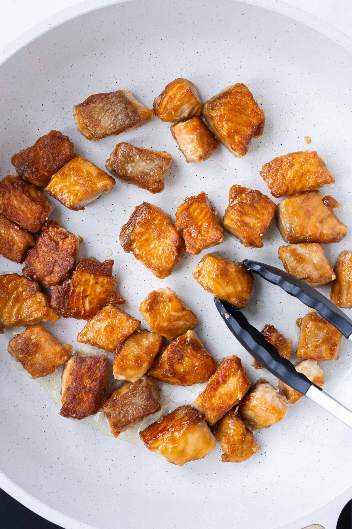 Seasoned salmon is cooked in a skillet.