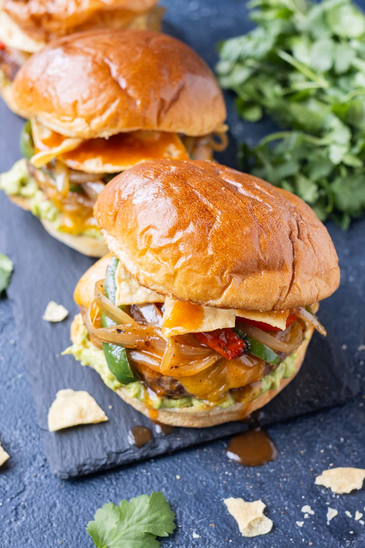 Three cheesy enchilada burgers are on a serving plate for a Taco Tuesday hamburger night.
