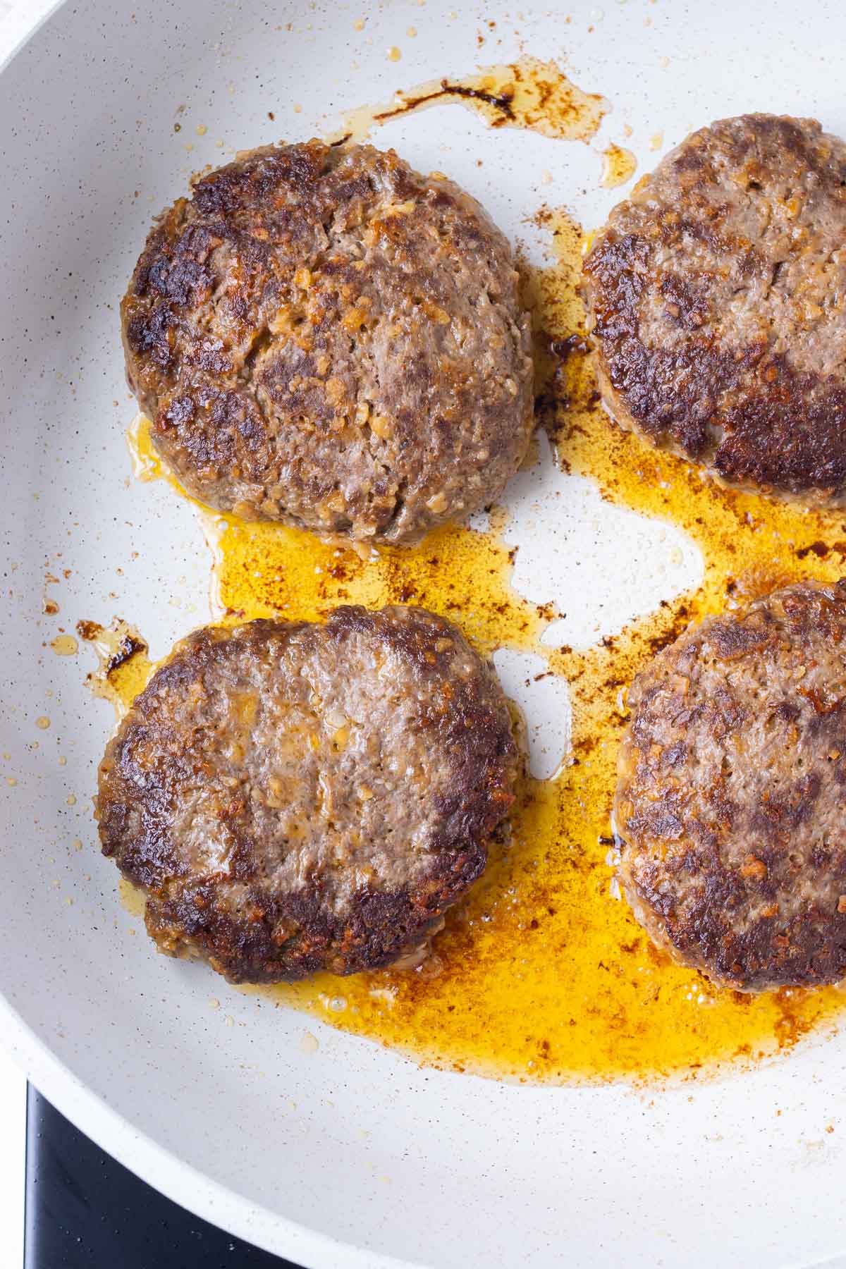 Enchilada burger patties are cooked in a skillet.