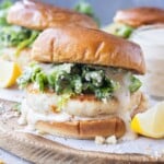 A Chicken Caesar Burger with salad dressing drizzled on top sits on a serving board next to a lemon wedge.