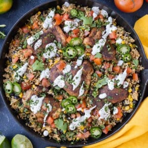 A skillet is full of a cilantro lime chicken and rice dish with sour cream and tomatoes on top.