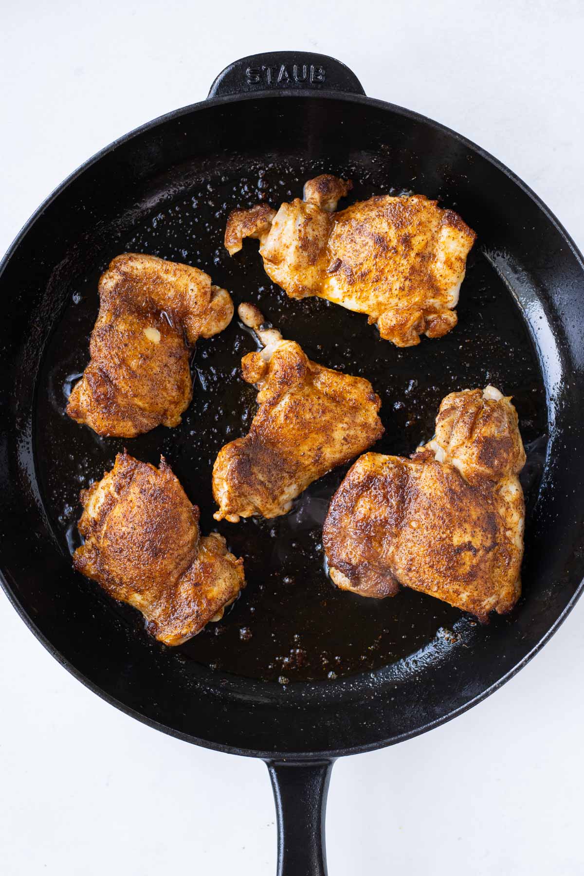 Seasoned chicken thighs are cooked in a skillet.