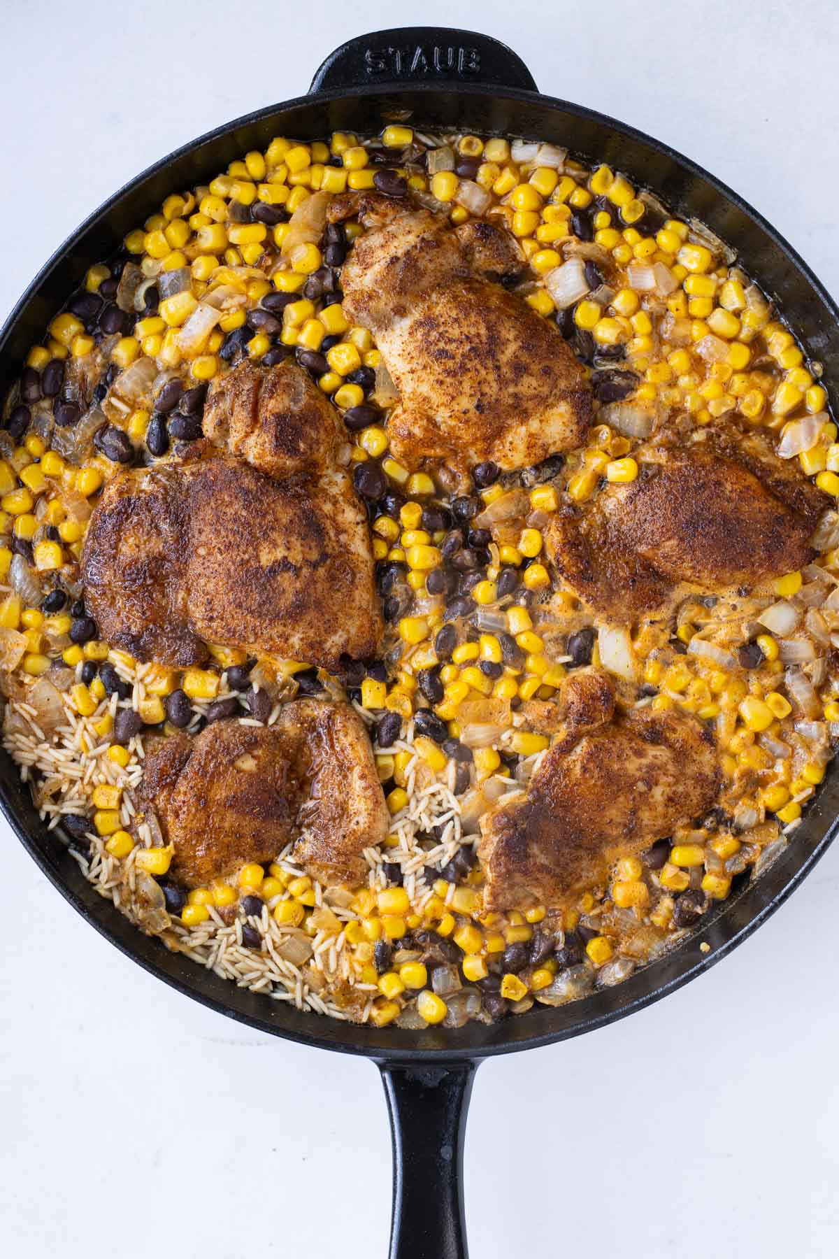 Chicken, corn, and black beans are added to the skillet with rice.
