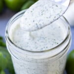 A spoon is scooping up some creamy cilantro lime dressing from a glass mason jar.
