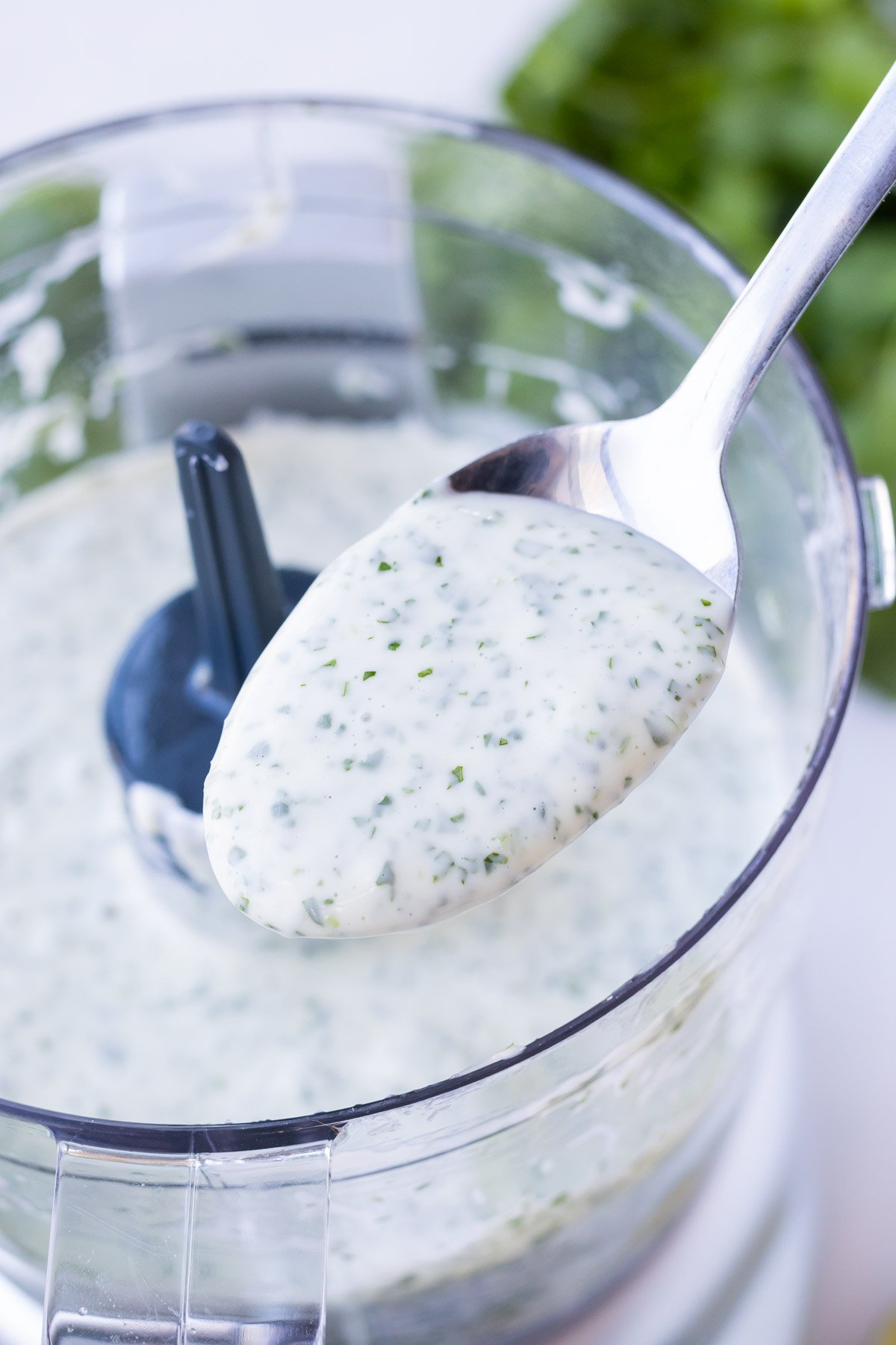 A spoon shows the texture of cilantro lime dressing from a food processor.