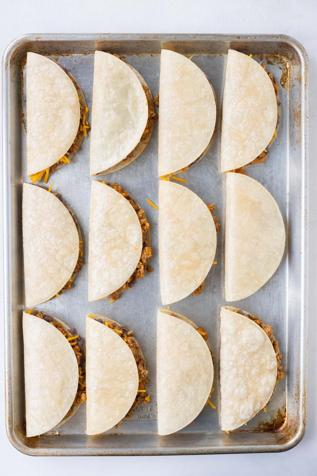 Filled ground turkey tacos are ready to bake on a tray.