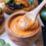 Gochujang mayo with sesame seeds is lifted out of a bowl with a wooden spoon.