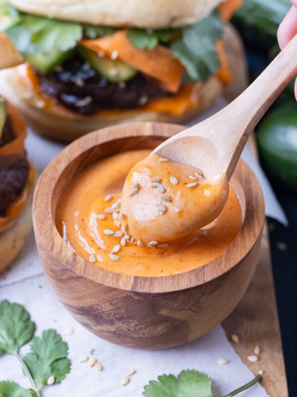 Gochujang mayo with sesame seeds is lifted out of a bowl with a wooden spoon.