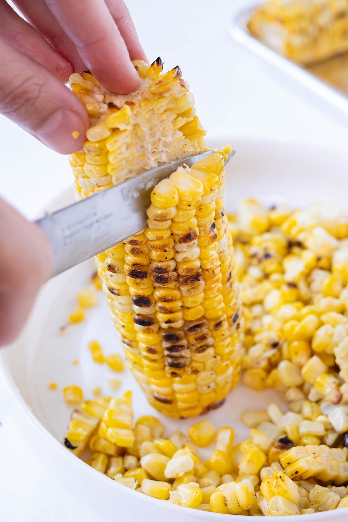A knife cuts corn away from the cob.