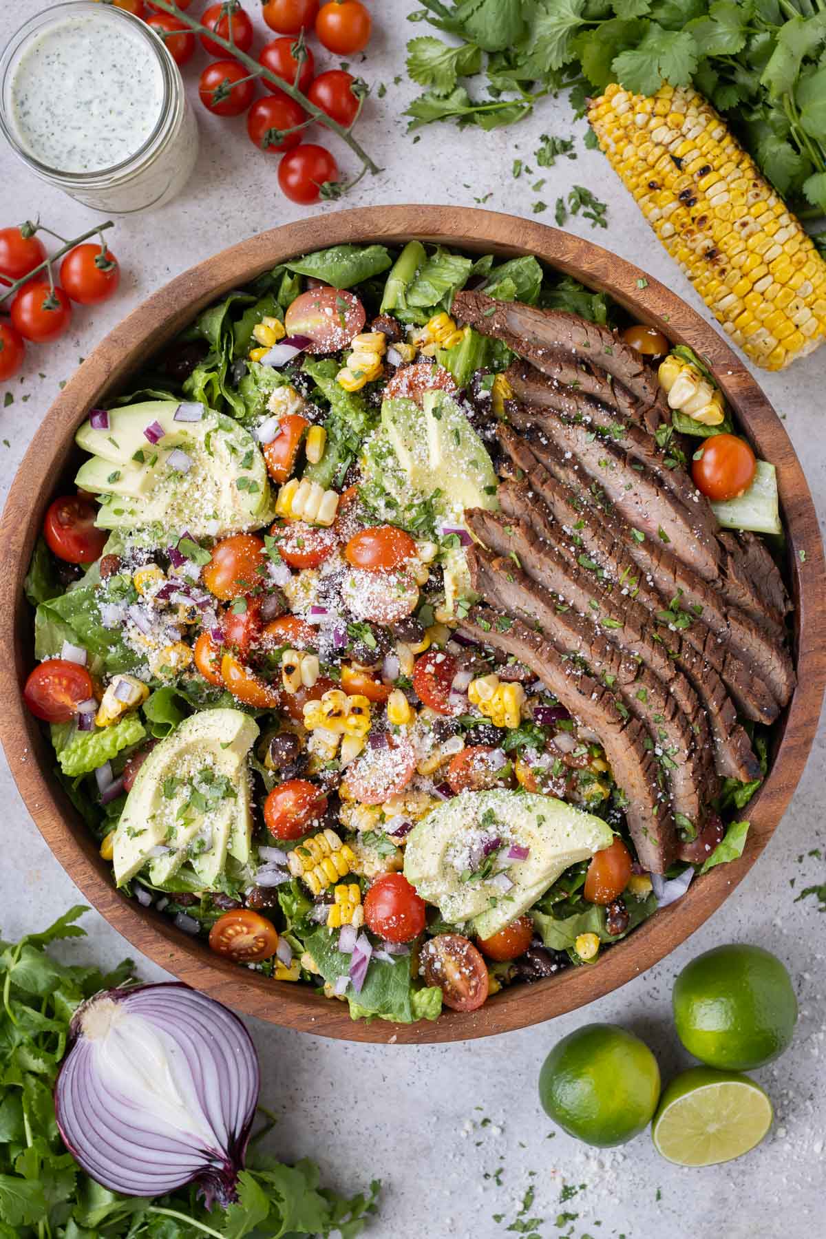 Fajita steak is layered on top of a salad with corn, tomatoes, avocados, and black beans.