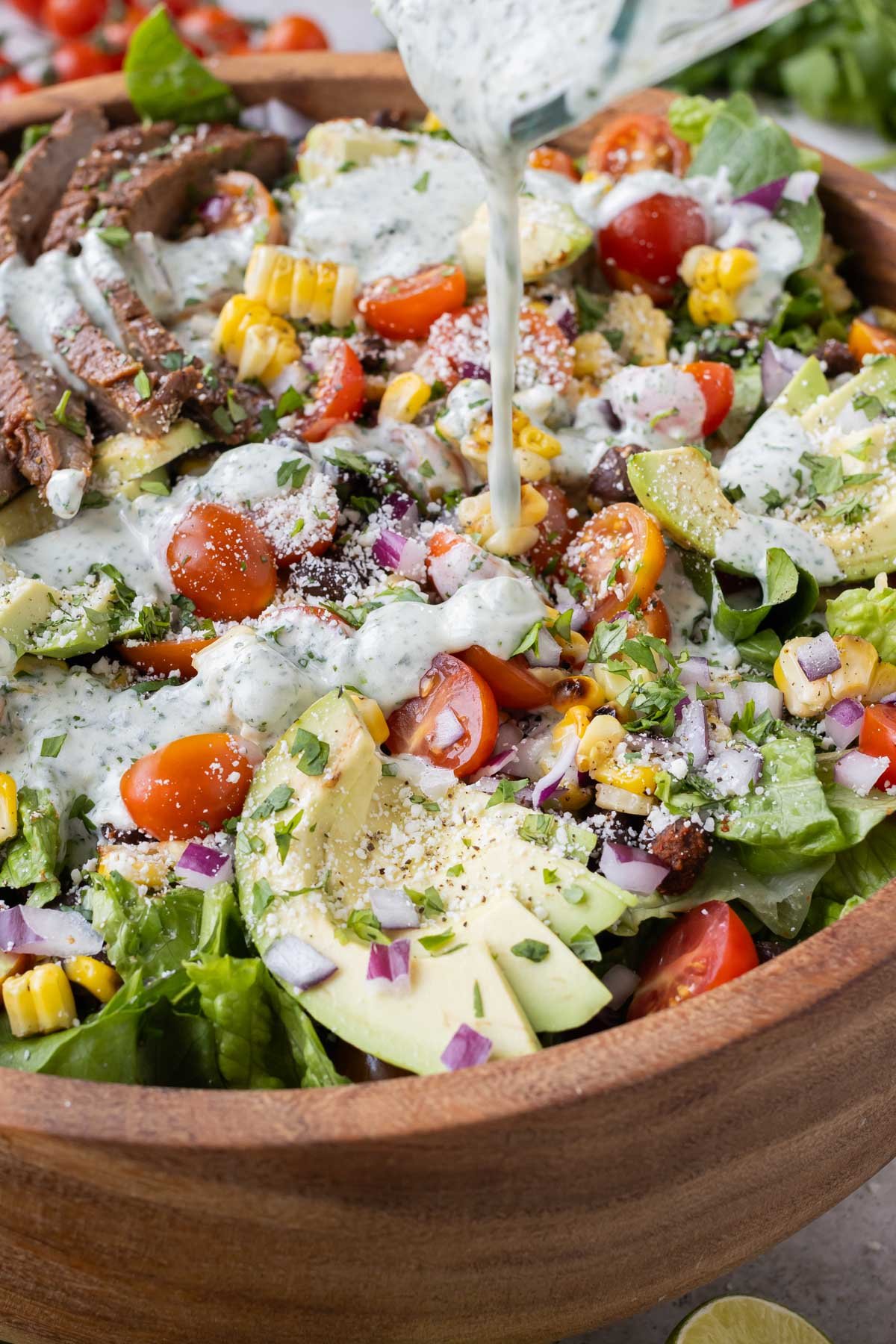 A creamy cilantro lime dressing is drizzled over a fajita steak salad with corn, tomato, and avocado.