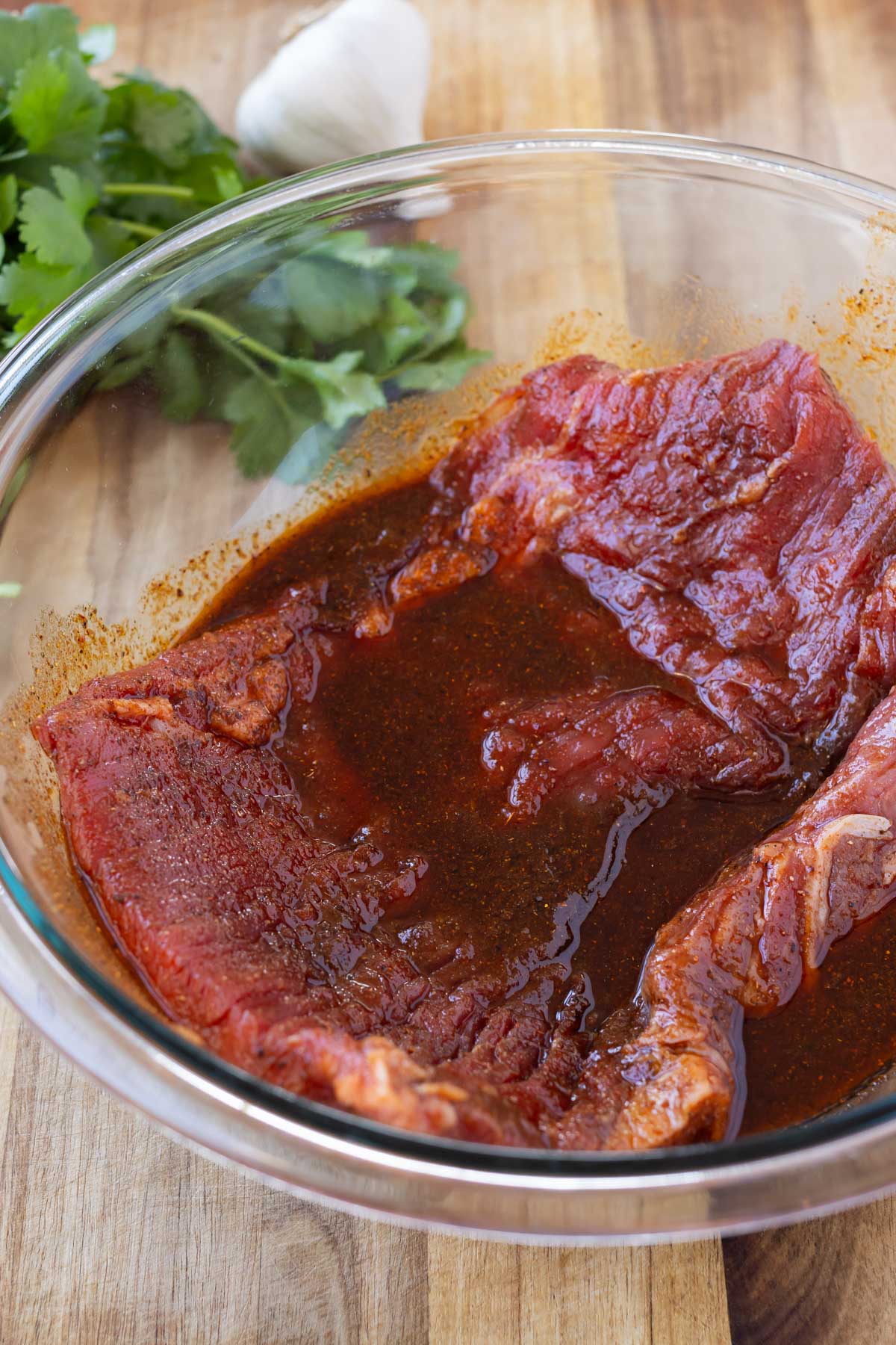 Flank steak is marinated in a glass bowl for a fajita salad.