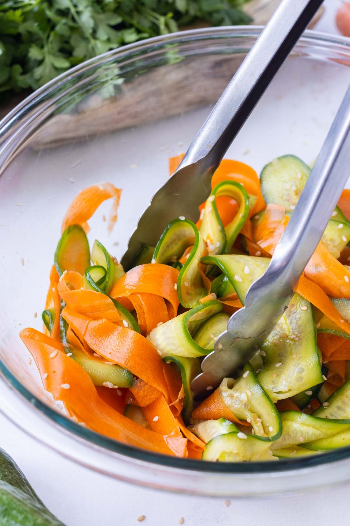 Tongs toss carrots and cucumber with a slaw dressing.