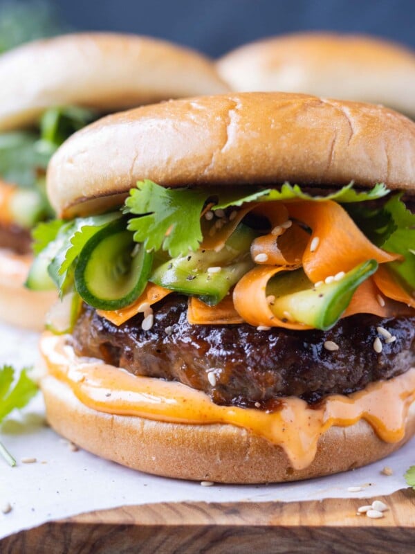 Korean Beef Burgers are served on a wooden tray with spicy gochujang mayo and a crisp pickled carrot and cucumber slaw.