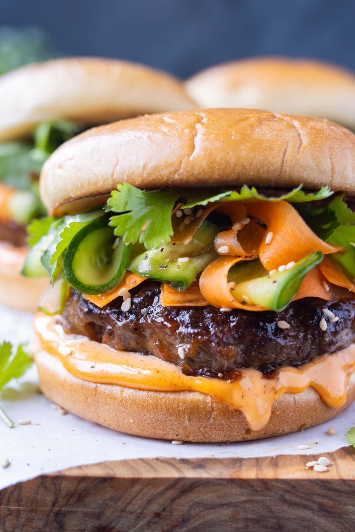 Korean Beef Burgers are served on a wooden tray with spicy gochujang mayo and a crisp pickled carrot and cucumber slaw.