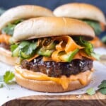 Korean Beef Burgers with gochujang mayo and a carrot cucumber slaw are served on a wooden tray.
