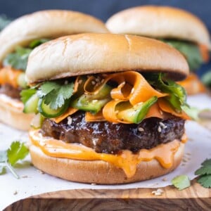 Korean Beef Burgers with gochujang mayo and a carrot cucumber slaw are served on a wooden tray.