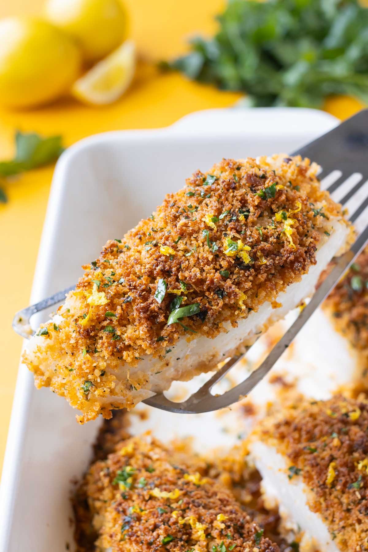A spatula lifts up a fillet of cod with a Parmesan-Panko crumb topping from a baking dish.