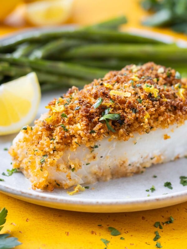 A fillet of Parmesan Crusted Cod is served on a plate with a lemon wedge and green beans.