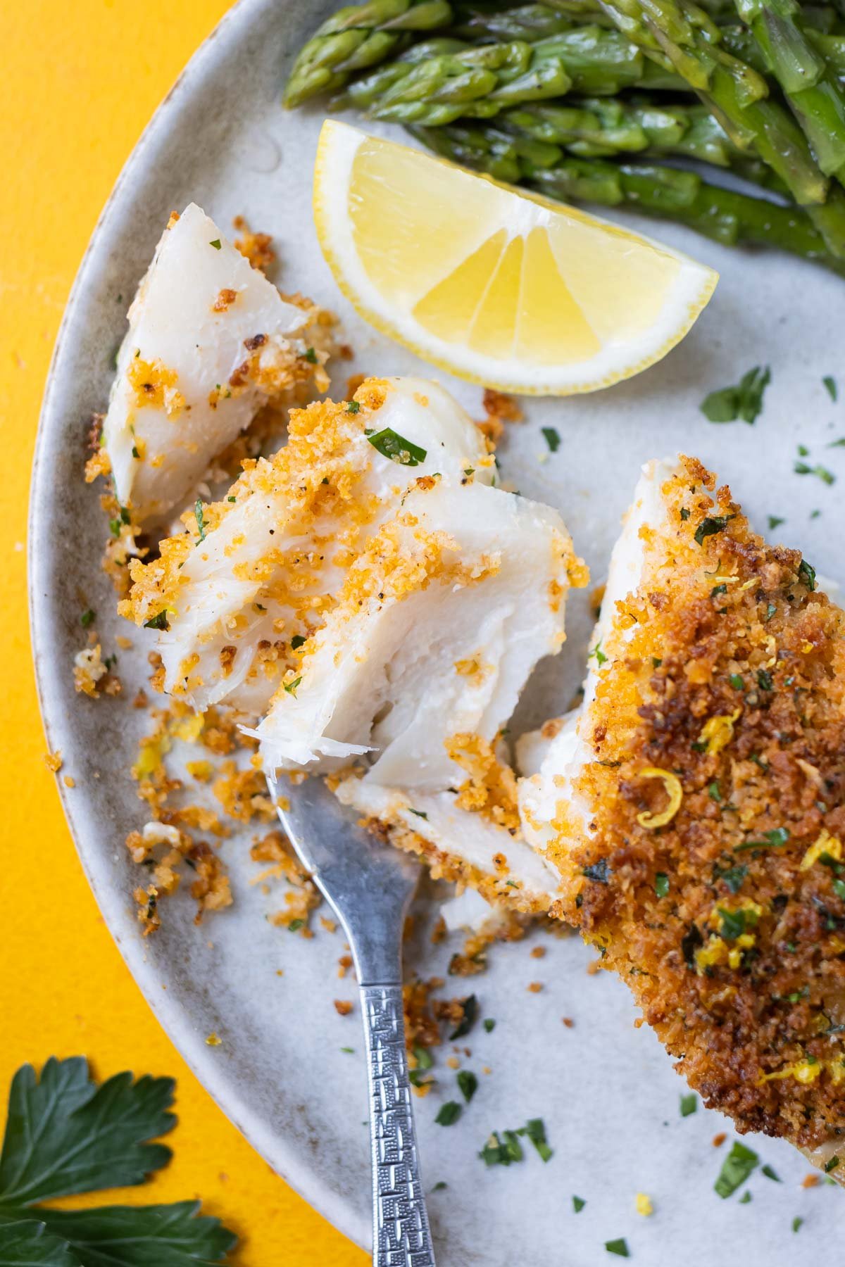 A fork scoops up a bite of Parmesan and panko crusted cod from a dinner plate.