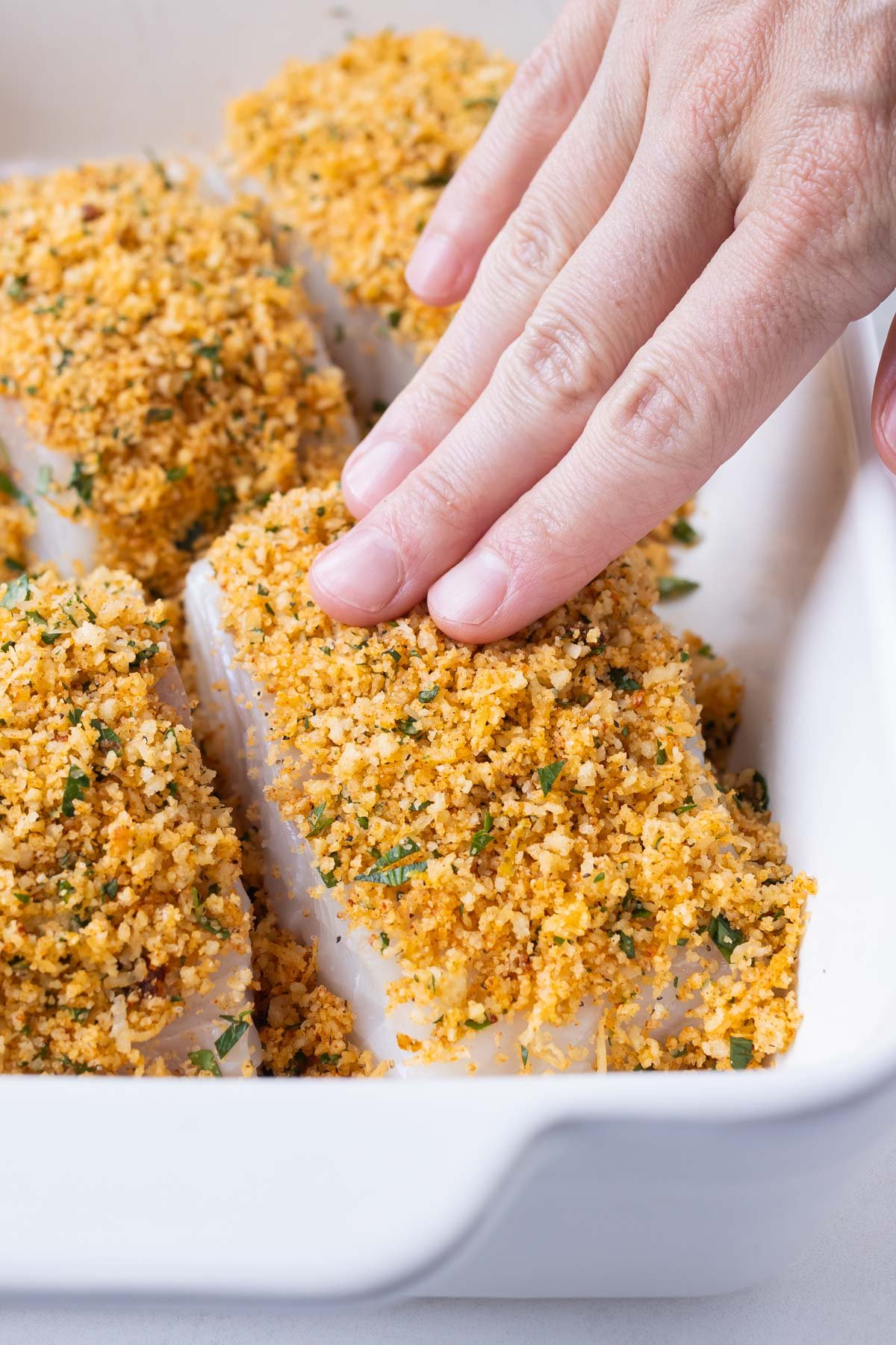 Fingers press a Parmesan and Panko coating into a filet of cod.