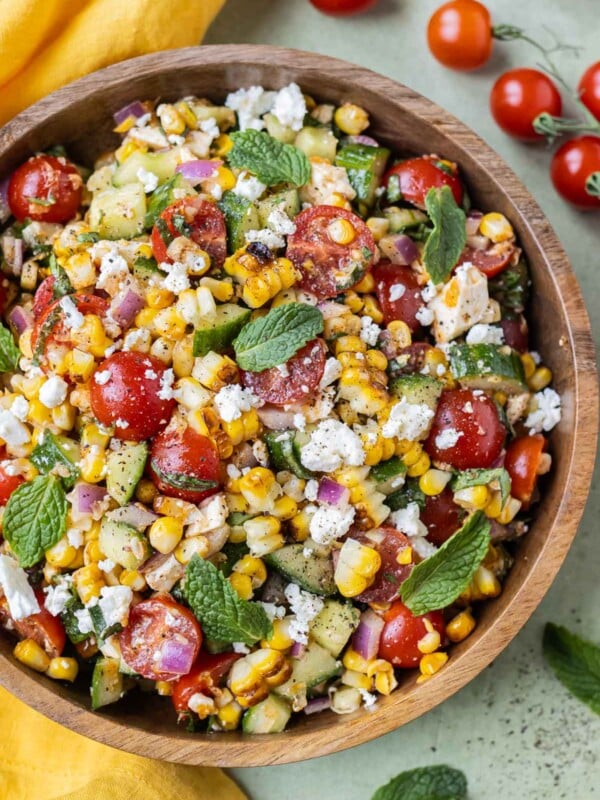 A roasted summer corn salad with tomatoes, feta, cucumber, and a homemade vinaigrette is served in a wooden bowl.