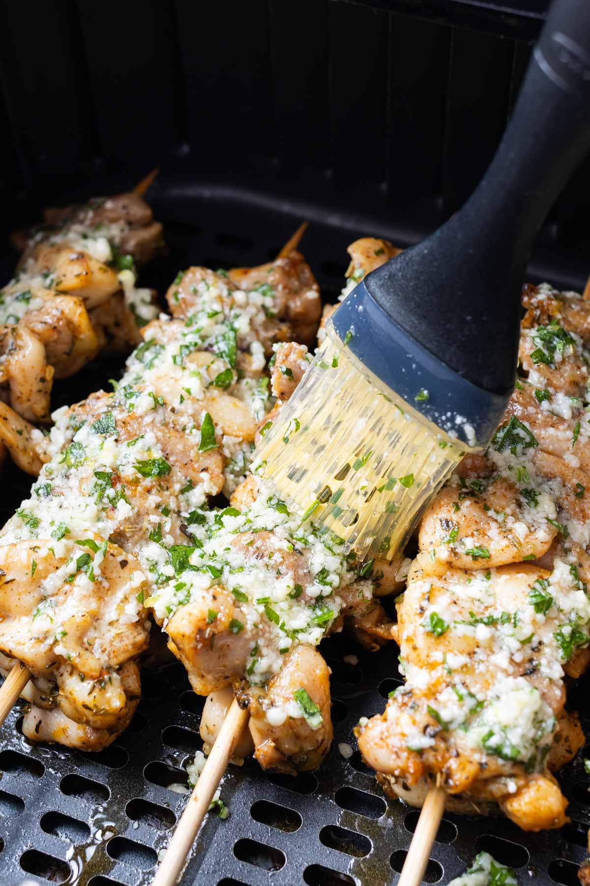 Garlic Parmesan sauce is brushed onto chicken thigh skewers in the air fryer.