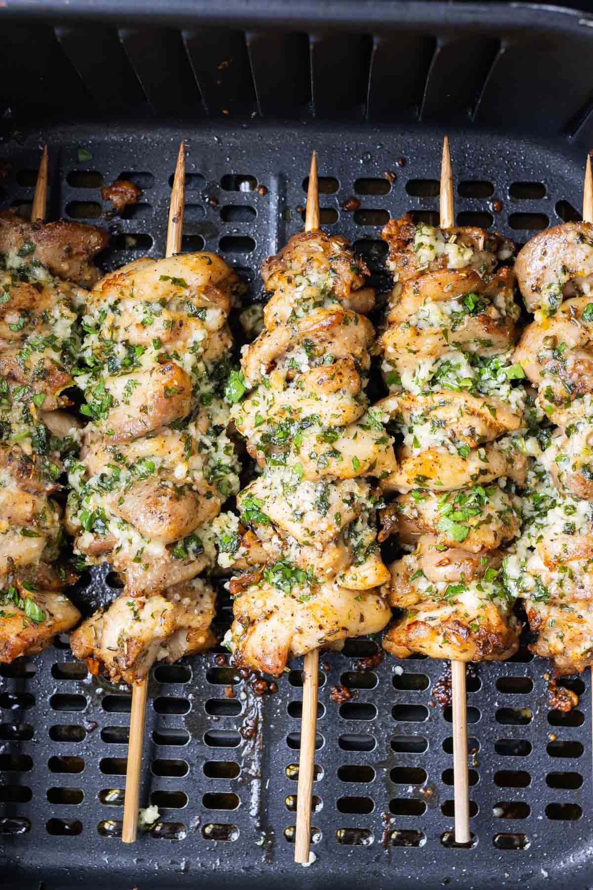 Chicken thigh skewers are in an air fryer basket with a garlic Parmesan butter.