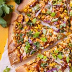 BBQ Chicken Pizza with summer corn, red onions, and barbecue sauce has been cut into slices for serving.