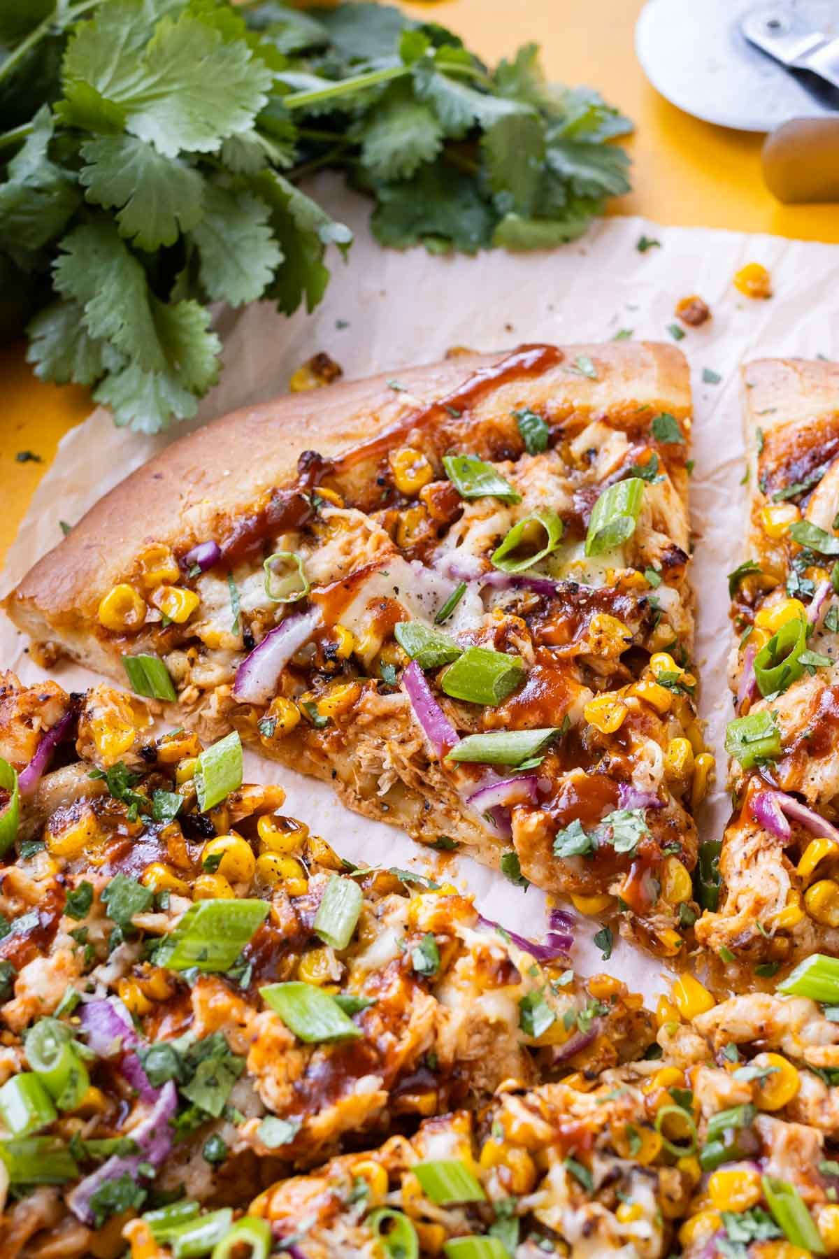 A slice of BBQ chicken pizza with roasted corn and red onions is on a piece of parchment paper.