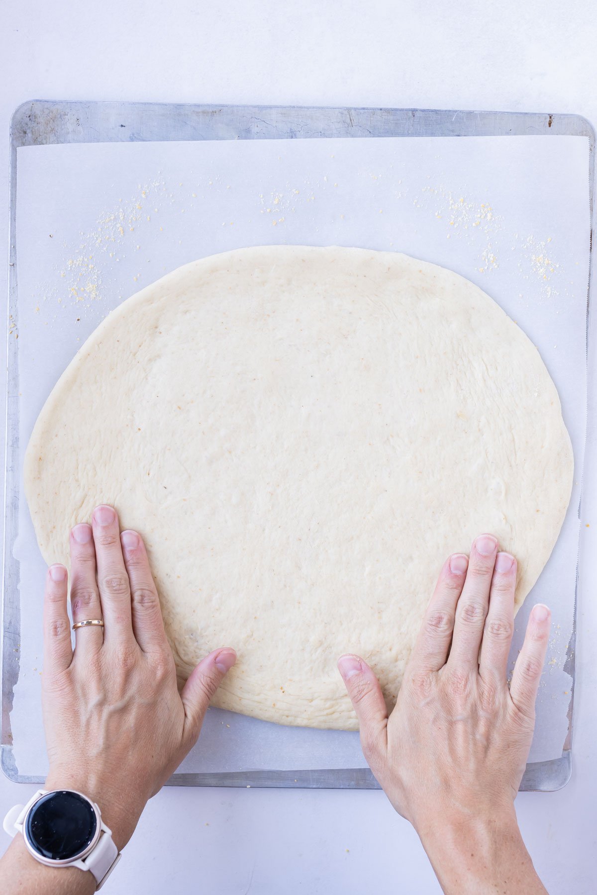 Hands flatten out a pizza dough and shape it.