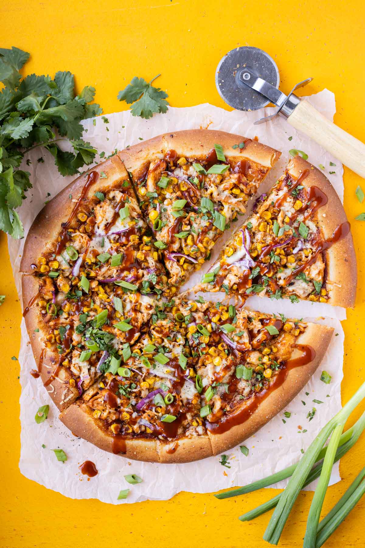 Cilantro and green onions are added to a bbq chicken pizza before serving.